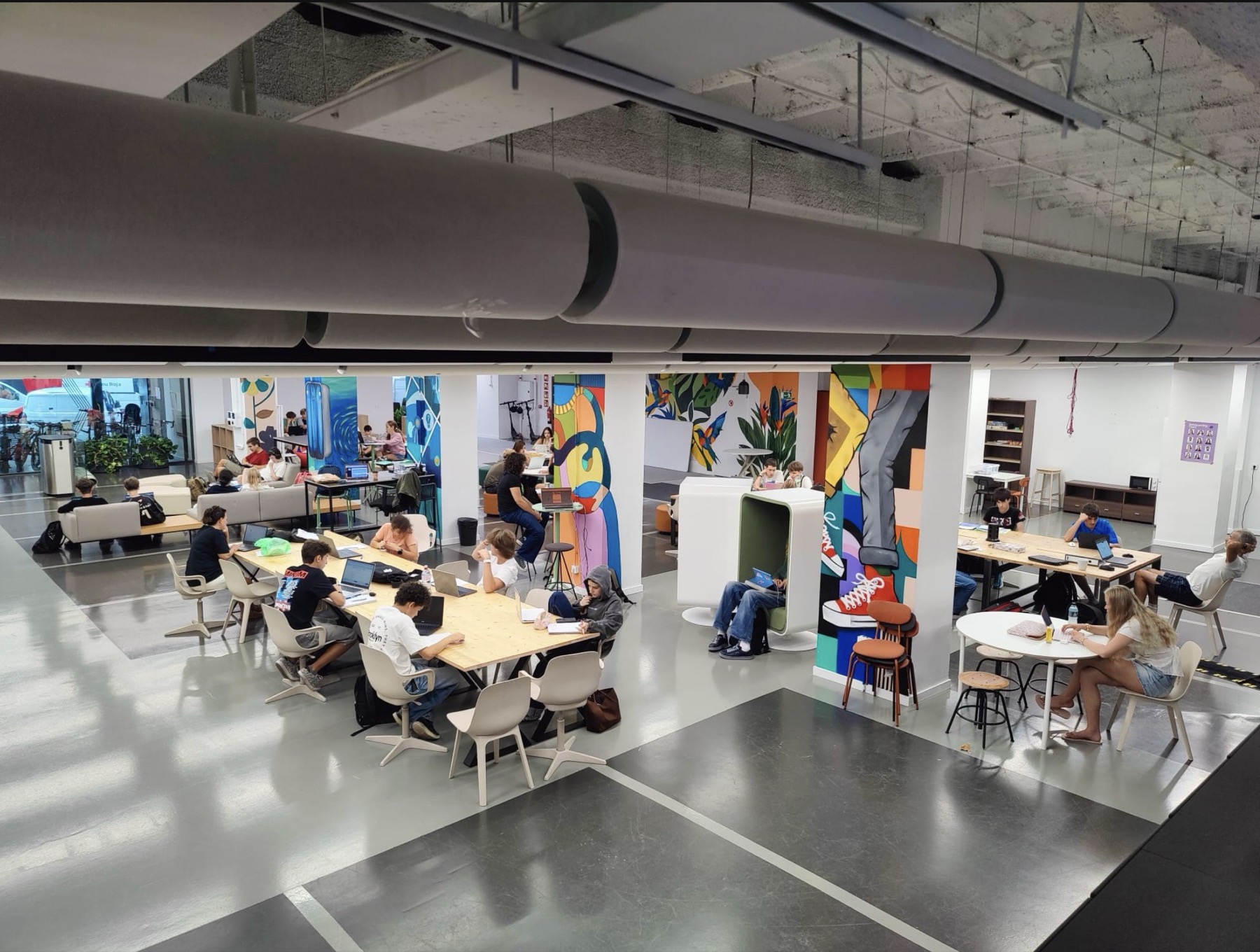 Same co-working space transformed with a colourful mural, students working at the tables