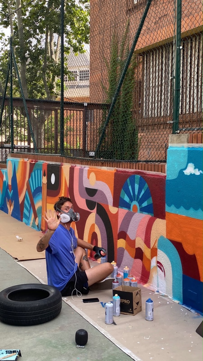 Matt painting a colourful abstract mural at a school